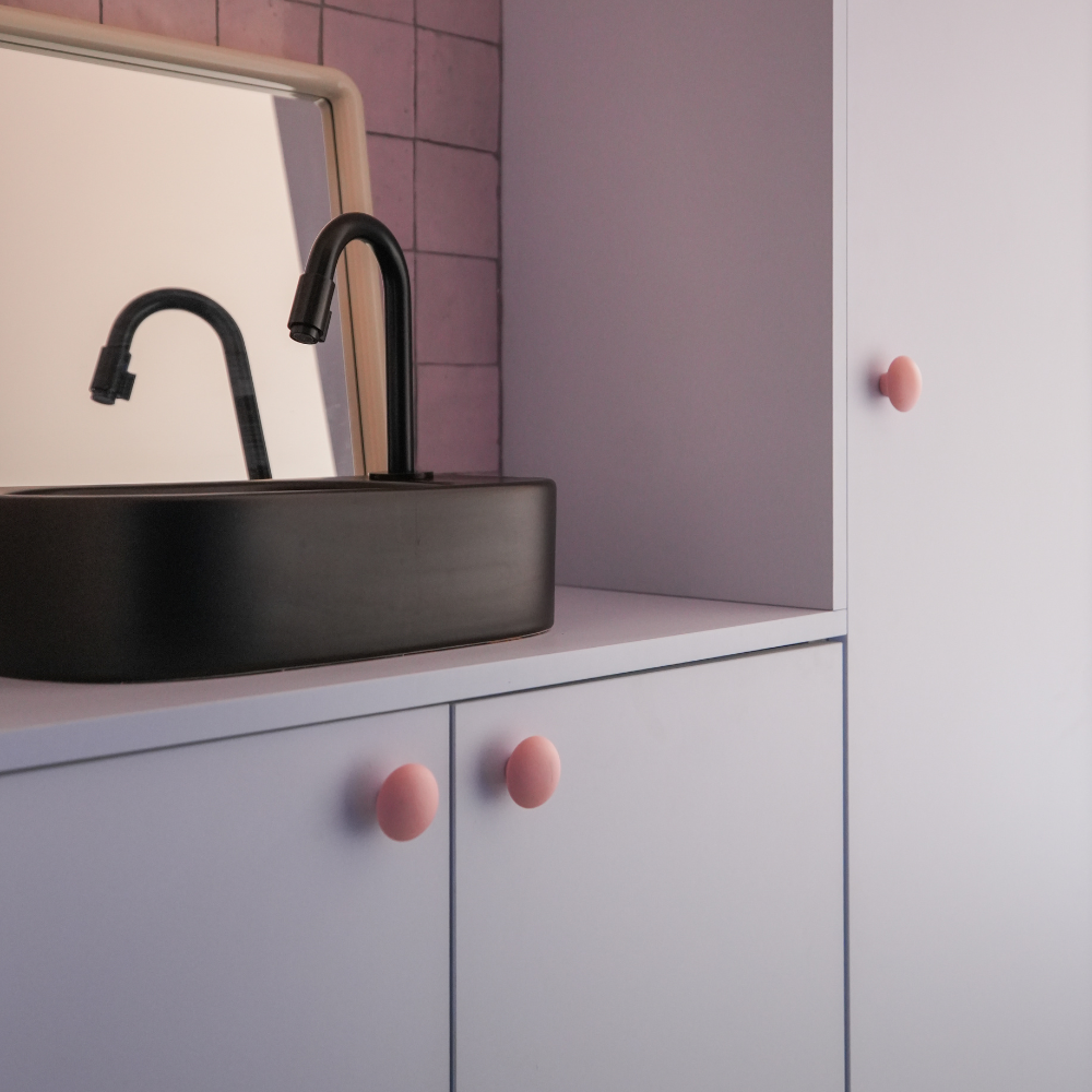 Boutons de meubles rose mat, posés sur  un meuble de salle de bain rose clair, créés avec des caissons Ikea Metod. Mitigeur et vasque noirs. Crédence en céramique rose.