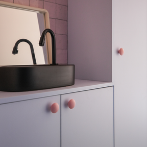 Boutons de meubles rose mat, posés sur  un meuble de salle de bain rose clair, créés avec des caissons Ikea Metod. Mitigeur et vasque noirs. Crédence en céramique rose.