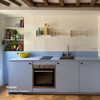 Petite cuisine linéaire basse aux façades et plan de travail bleu clair, coloris "Piscine" Studio Couleur. Caissons Ikea Metod. Poignées bordeaux.