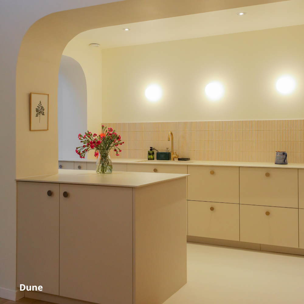 Cuisine ouverte beige coloris "Dune" Studio Couleur, posée sur des caissons Ikea Metod. Plan de travail linéaire et ilot central en quartz. Crédence beige en céramique, entrée de de la cuisine en porte arrondie.