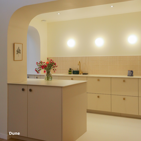Cuisine ouverte beige coloris "Dune" Studio Couleur, posée sur des caissons Ikea Metod. Plan de travail linéaire et ilot central en quartz. Crédence beige en céramique, entrée de de la cuisine en porte arrondie.