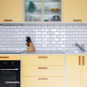 Cuisine linéaire aux portes et façades de tiroirs Studio Couleur jaunes, poignée en bois et caissons Ikea Metod. Crédence en céramique et plan de travail blanc.