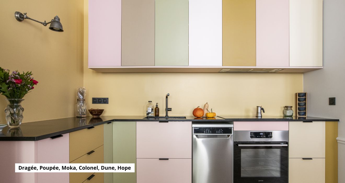 Réalisation Studio Couleur. Cuisine en L multicolore, façades roses, beiges, et jaunes. Plan de travail noir. Caissons Ikea Metod.
