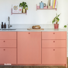 Petite cuisine linéaire basse, aux portes et façades de tiroir rose saumon, poignées roses et plan de travail en céramique gris