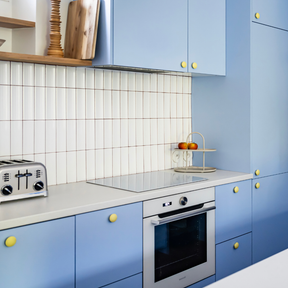 Cuisine Ikea Metod aux portes bleu clair coloris "Piscine" Studio Couleur, et boutons de porte jaune mat. Crédence en céramique et plan de travail blanc.
