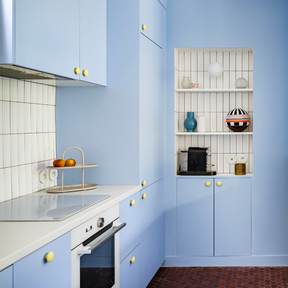 Cuisine Ikea Metod aux portes bleu clair coloris "Piscine" Studio Couleur, et boutons de porte jaune mat. Crédence en céramique et plan de travail blanc.
