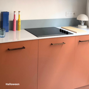 Petite cuisine avec caissons bas uniquement, aux façades orange coloris "Halloween" Studio Couleur. Plan de travail blanc et crédence bleue.