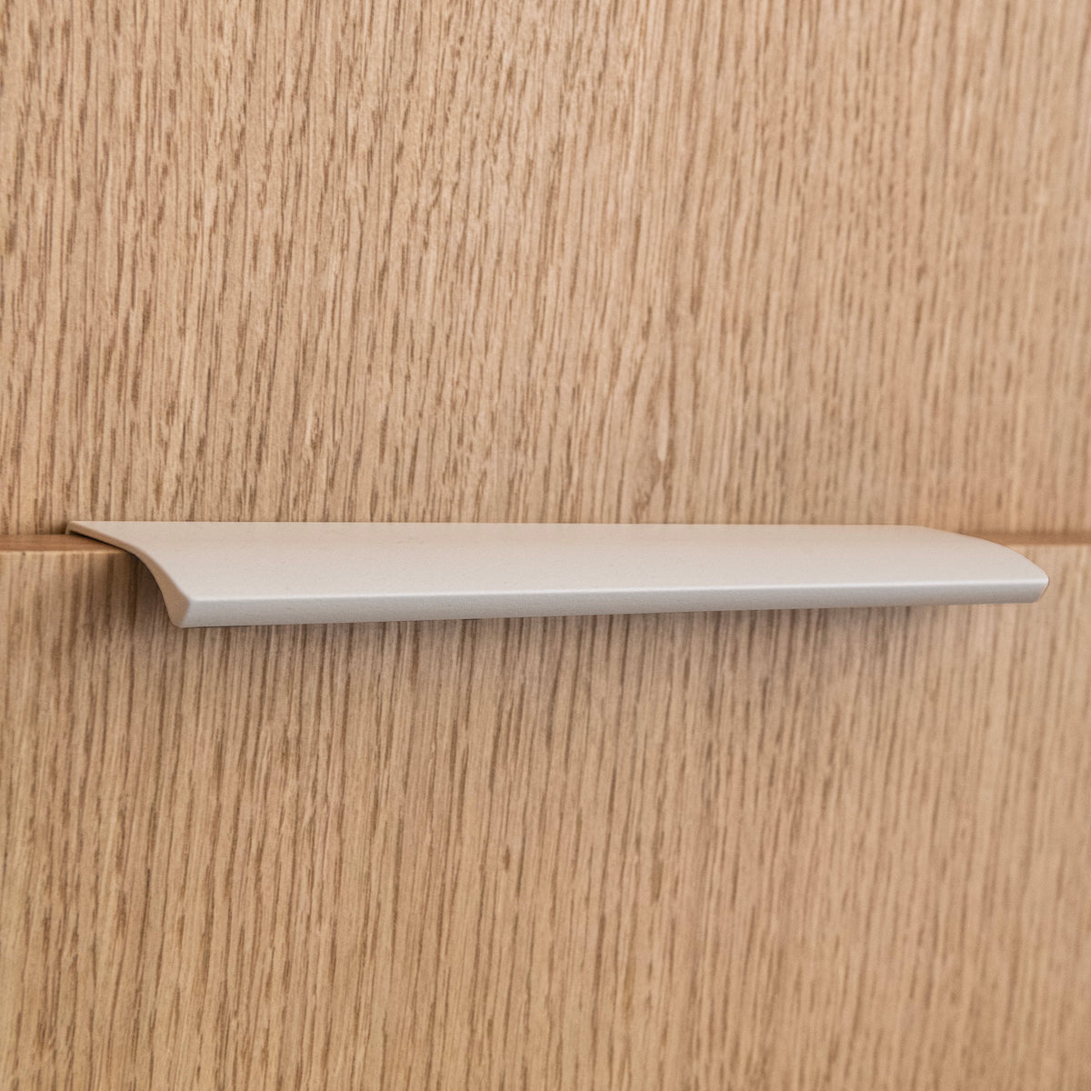 Poignée profilée pour meuble coloris beige, de 20cm de longueur. Elle se fixe discrètement sur le rebord des portes de cuisine et d'armoires.