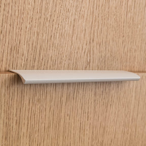 Poignée profilée pour meuble coloris beige, de 20cm de longueur. Elle se fixe discrètement sur le rebord des portes de cuisine et d'armoires.