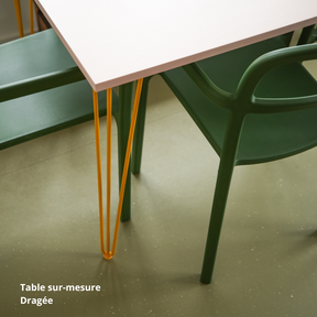 Table de salle à manger rose clair créée sur-mesure avec des panneaux Studio Couleur. Pieds de table jaune-orangé et chaises vertes. Sol vert moucheté.
